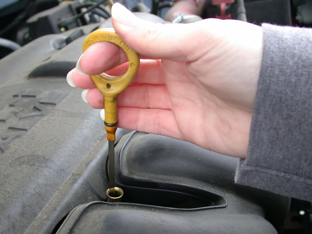 Jauge d’huile moteur marquée « ENGINE OIL », tenue à la main.
