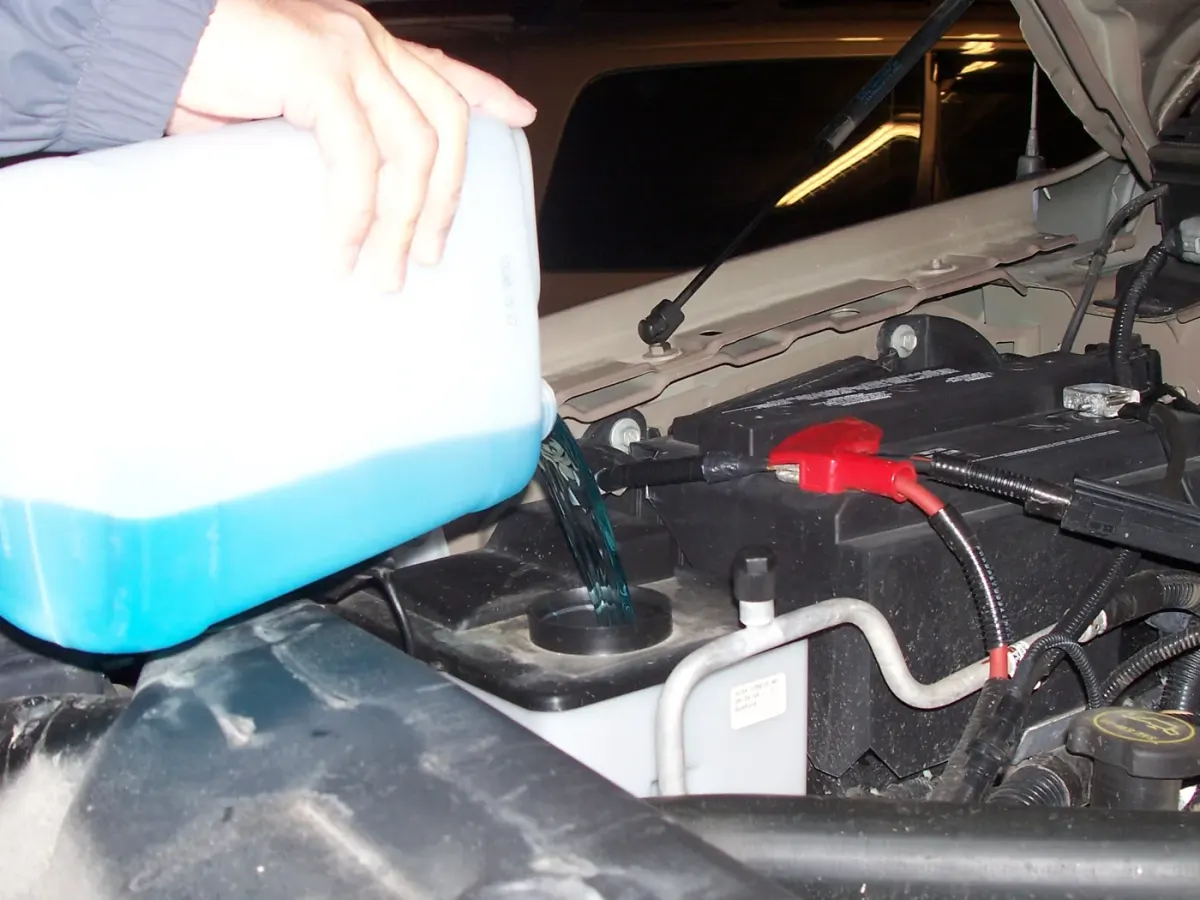 Personne versant du liquide lave-glace bleu dans son réservoir.