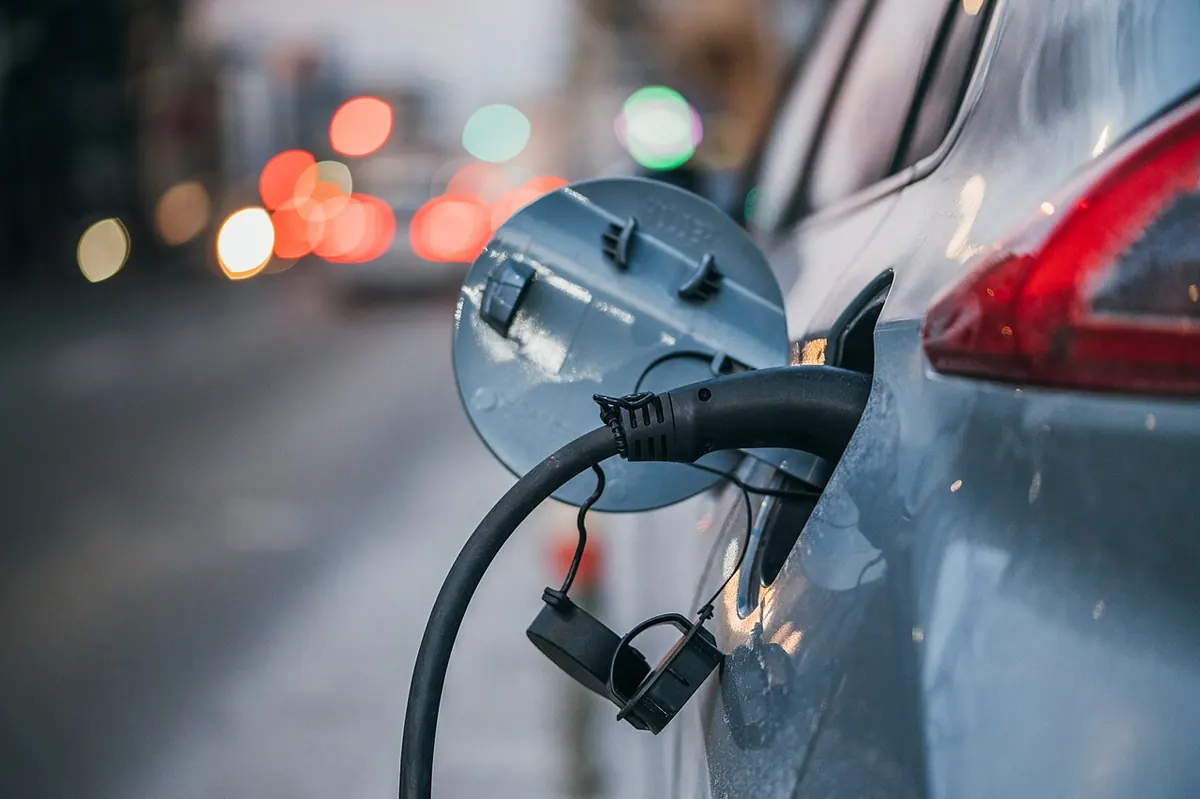 Câble de recharge branché sur la prise d’une voiture électrique, en ville.