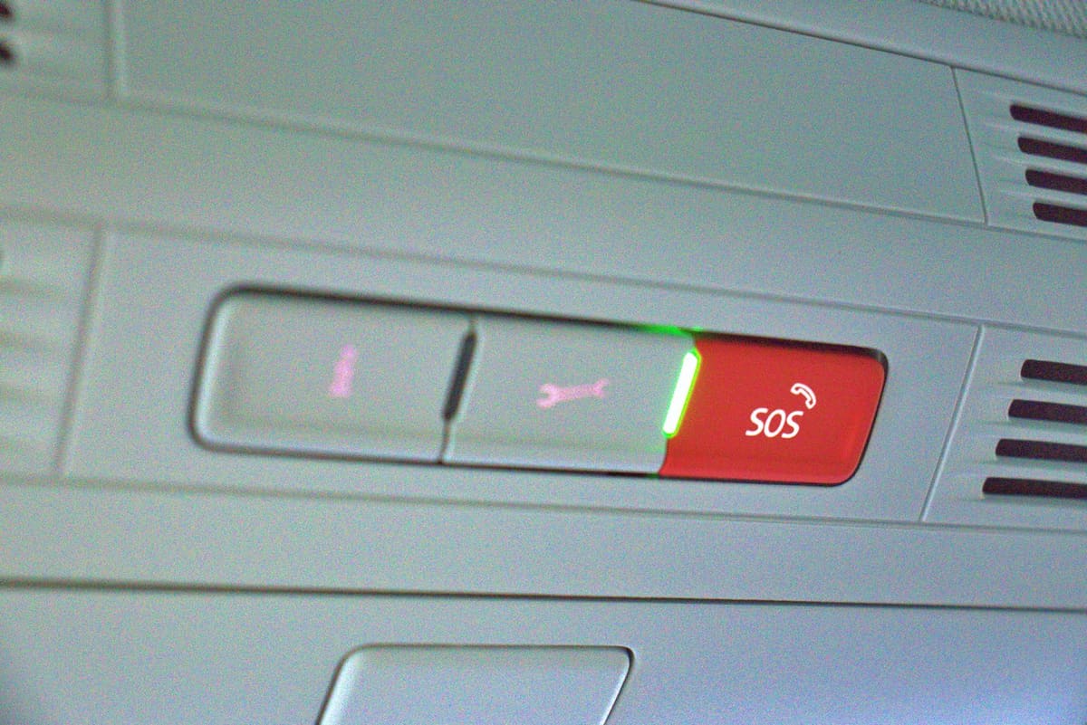 Bouton rouge SOS avec pictogramme téléphone au plafond d’une voiture, à côté d’un bouton distinct d’assistance.