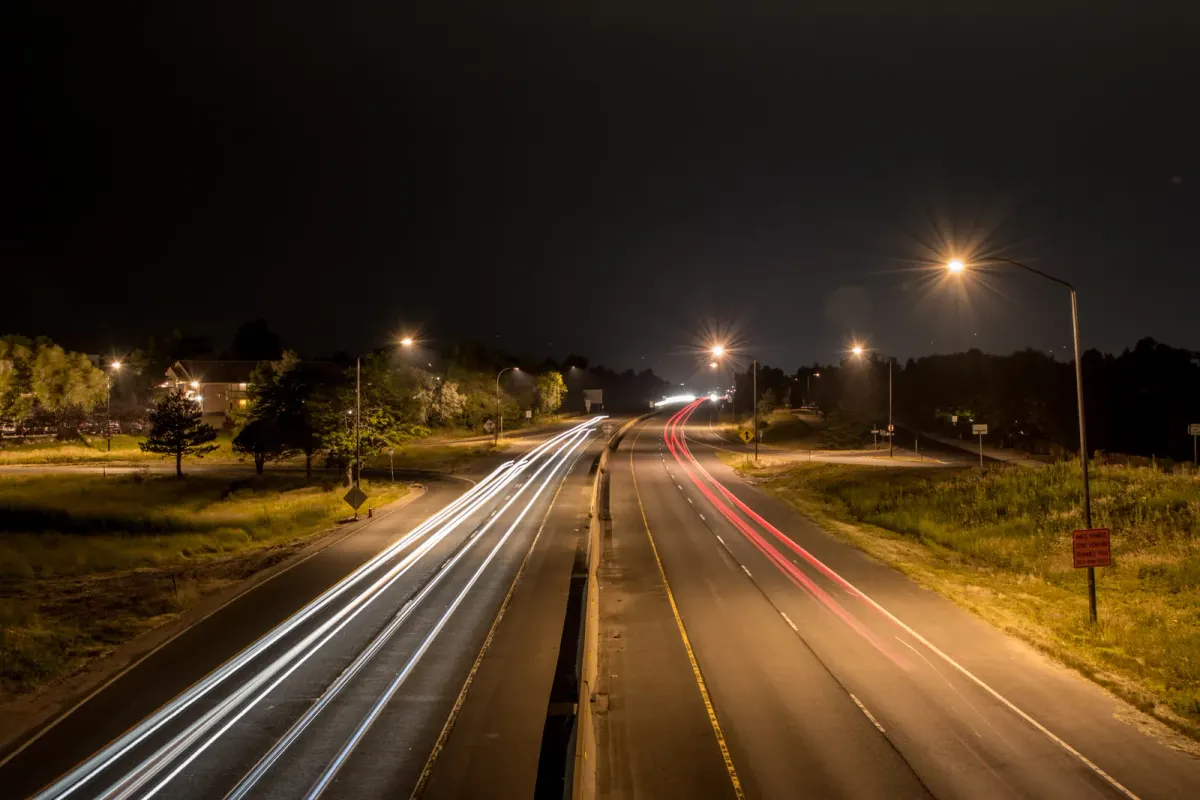 Traînées lumineuses de véhicules photographiées de nuit en pose longue, phares blancs dans un sens et feux rouges dans l’autre.