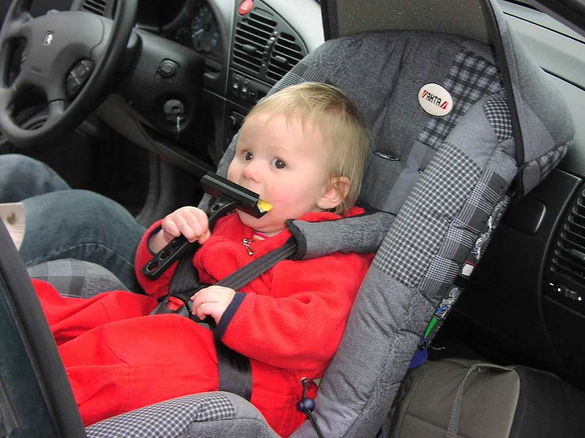 Jeune enfant attaché dans un siège auto installé dos à la route sur la place passager avant.